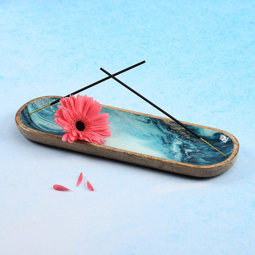 Blue marble incense holder with wood frame—two burning sticks, pink gerbera flower, and scattered petals for calming aromatherapy display