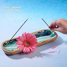 Green marble incense holder with wood frame—two incense sticks being lit, pink daisy flower, and scattered petals for calming aromatherapy
