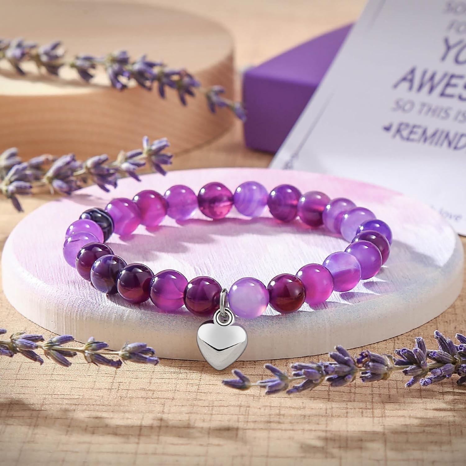 Purple beaded bracelet with silver heart charm—displayed on wooden platform with lavender sprigs and gift box, perfect for spa gift sets and meaningful jewelry gifts