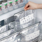 Hand placing labeled reusable aluminum food storage bag into refrigerator drawer, surrounded by organized silver bags with seafood and meat illustrations, designed for eco-friendly meal prep and freshness.